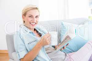 Pretty blonde woman reading a book and holding a mug