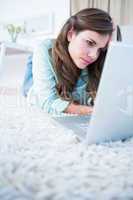 Focused woman using her laptop lying on the floor
