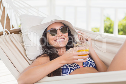 Pretty brunette relaxing on a hammock and drinking orange juice