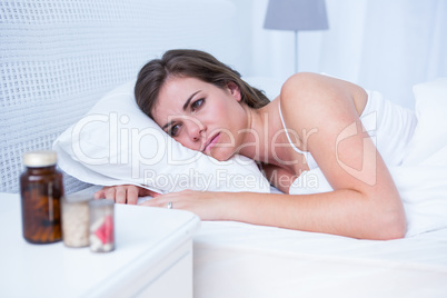 Sad woman looking at pills in bed