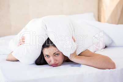 Pretty brunette looking at camera and hiding under the pillow