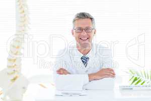 Doctor sitting at his desk smiling at camera