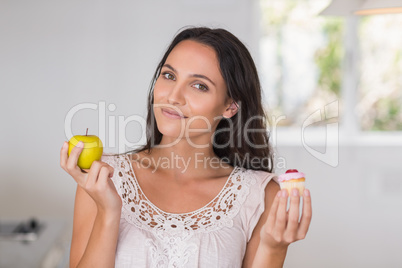 Beautiful brunette holding mini cupcake and an apple