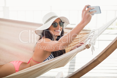 Pretty brunette relaxing on a hammock and taking selfie