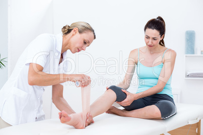 Doctor bandaging her patient ankle