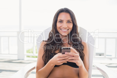 Pretty brunette sitting on a chair and texting with her mobile p