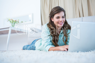 Pretty brunette using her laptop lying on the floor