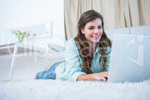 Pretty brunette using her laptop lying on the floor