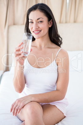 Pretty brunette holding a glass of water on bed