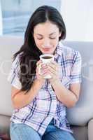 Pretty brunette holding coffee mug on couch