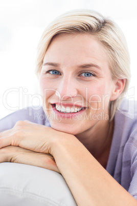 Pretty blonde woman sitting on the couch and smiling at the came