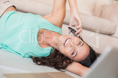 Pretty brunette lying on the floor and using her mobile phone