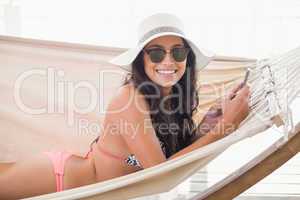 Pretty brunette relaxing on a hammock and texting with her mobil