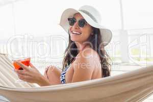 Pretty brunette relaxing on a hammock and drinking cocktail