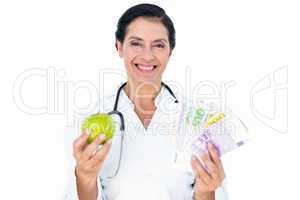 Confident female doctor holding green apple and banknotes