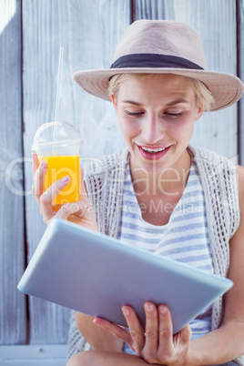 Pretty blonde woman using her tablet and holding orange juice