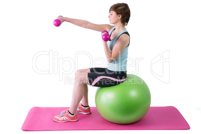 Pretty brunette exercising with dumbbells on fitness ball