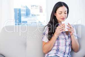 Pretty brunette holding hot beverage on couch