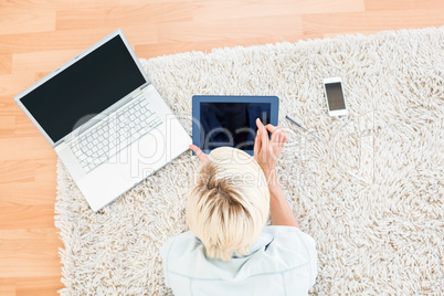 Pretty blonde woman lying on the floor and using her tablet