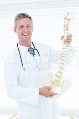 Doctor holding anatomical spine and smiling at camera