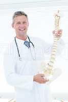 Doctor holding anatomical spine and smiling at camera
