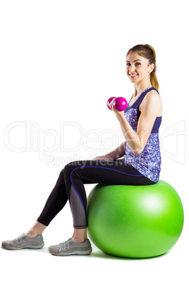 Fit woman lifting dumbbell sitting on ball