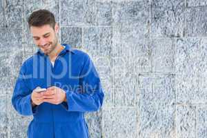 Composite image of male mechanic text messaging through mobile p