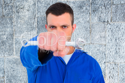 Composite image of confident male mechanic holding spanner