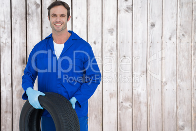 Composite image of confident mechanic holding tire