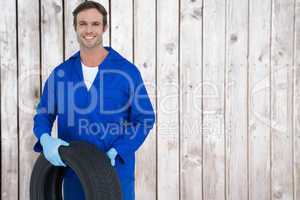 Composite image of confident mechanic holding tire