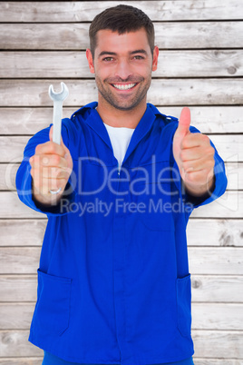 Composite image of smiling mechanic holding spanner while gestur