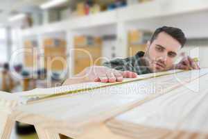 Composite image of worker measuring wooden plank