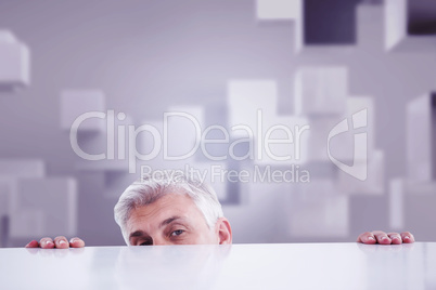 Composite image of businessman peeking over desk