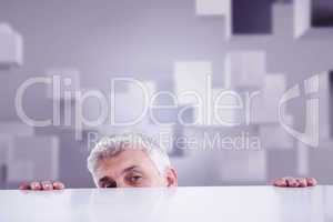 Composite image of businessman peeking over desk