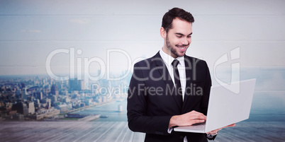 Composite image of smiling businessman standing and using laptop