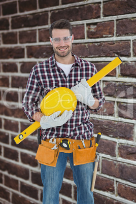 Composite image of handyman holding hard hat and spirit level