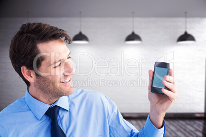 Composite image of smiling businessman showing smartphone to cam