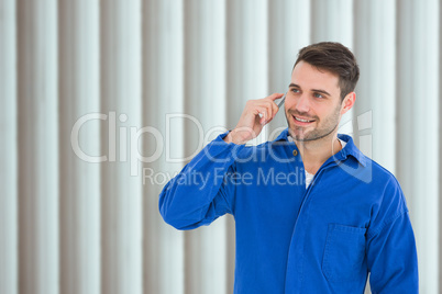 Composite image of happy young male mechanic using mobile phone