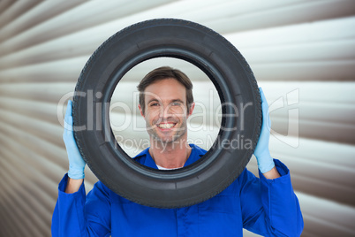 Composite image of confident mechanic looking through tire