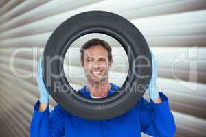 Composite image of confident mechanic looking through tire
