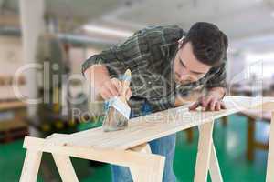 Composite image of worker using brush on wooden plank