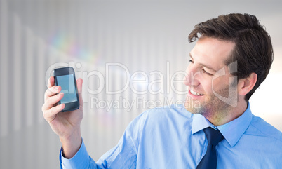 Composite image of smiling businessman showing smartphone to cam