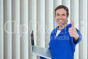 Composite image of mechanic holding laptop while showing thumbs