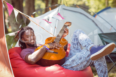 Happy hipster relaxing on campsite playing guitar