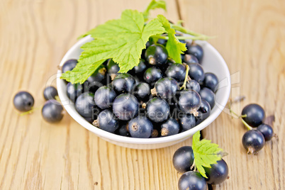 Black currants in bowl with leaf on board