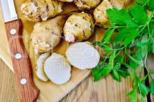 Jerusalem artichokes cut with knife and parsley on board