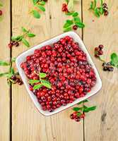Lingonberry red with leaves in bowl on board