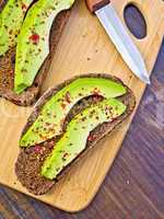 Sandwich with avocado and knife on board