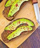 Sandwich with avocado and knife on dark board