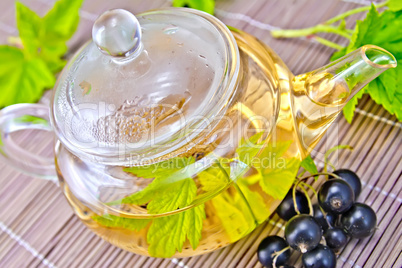 Tea with black currants in glass teapot on bamboo napkin